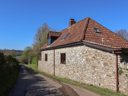 A stone cottage with a tiled roof along a narrow country road at Garden Cottage in Upottery