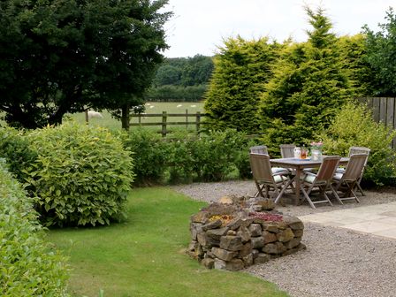 A garden with outdoor wooden table and chairs surrounded by bushes and trees at Badger in Little Thirkleby near Thirsk