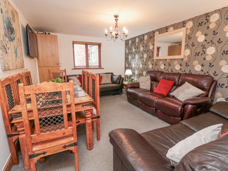 A living room with wooden dining table and chairs brown leather sofas a large floral wallpaper and a mirror at Psalm Cottage in Scarborough