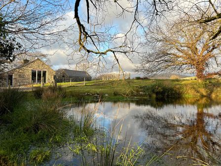 A stone house near a pond with grass trees and a fence at Hafod Y Llyn in Morfa Bychan near Porthmadog