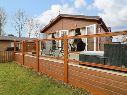 An outdoor patio with chairs and a sofa enclosed by a glass and wood railing at The Lake House in Marston near Barkston