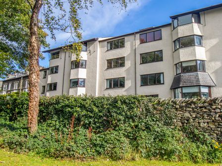 Exterior view of a multi-storey residential building with multiple windows and bay windows behind a stone wall and greenery at Newlands in Windermere