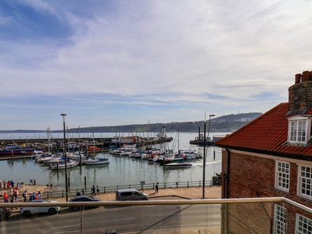 A view of a harbor with boats docked and people walking along the waterfront near a building with a red tiled roof at Apartment 2 in Scarborough