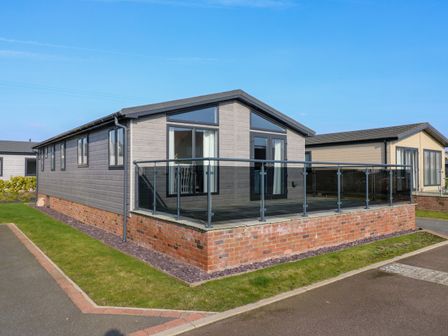 A modern single story house with glass balcony on brick base in a residential area at Number 43 The Poplars Burnham Market