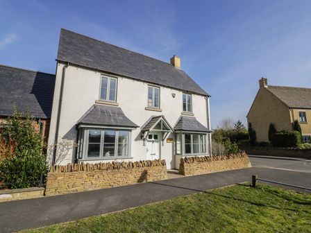 A two-story house with stone walls and slate roof behind a low stone wall at 2 Summers Way in Moreton-In-Marsh