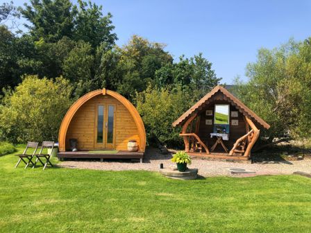 Two small wooden cabins on a grassy area with trees in the background at River View Pod near Muff County Donegal