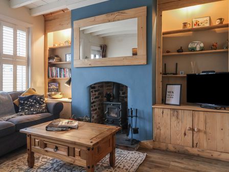 A living room with a wood stove fireplace a wooden coffee table and a sofa at Lychgate View Cottage in Aldbrough