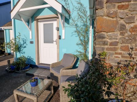 An outdoor seating area with wicker chairs and a glass table in front of a blue house with a white door at The Hollybush in Jeffreyston near Kilgetty