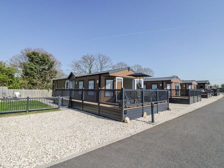 A row of wooden cabins with fenced porches along a paved road and gravel areas at Casa De Rhu in Evesham