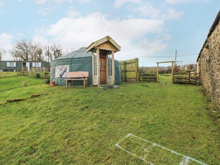 A grassy outdoor area with a yurt wooden bench and fence at Blaidd Bach in Carmarthen