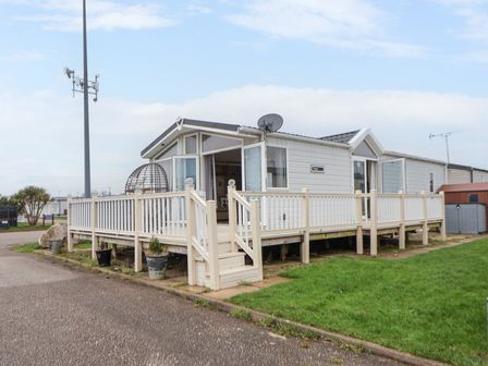 A mobile home with a fenced wooden deck and steps in a residential area at Hazel Park Lodge HP4 in Rhyl