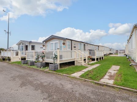 A row of beige mobile homes with white railings and steps on a grassy area at Hazel Park 11 HP11 in Rhyl