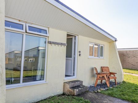 The outside of a single-story building with a door open and wooden chairs on gravel at Atlantic Escape in Widemouth Bay