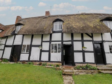 A thatched roof cottage with black timber framing windows flower beds and lawn at Church View in Welford-On-Avon