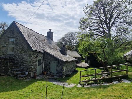 A stone cottage with a slate roof and green doors surrounded by grass and trees at Old Ty'n Y Wern in Rhosygwalia near Bala