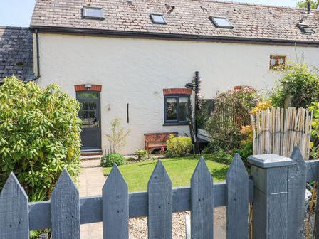 A garden with a wooden bench and plants in front of a white house with a blue door and windows at 3 The Barn in Haverfordwest