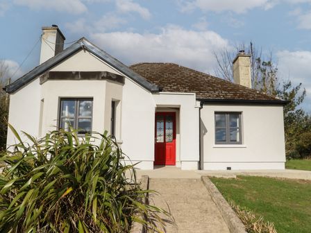 A single story house with white walls a red door and two windows with plants in front at Heatherbell House Ballyhoura near Buttevant