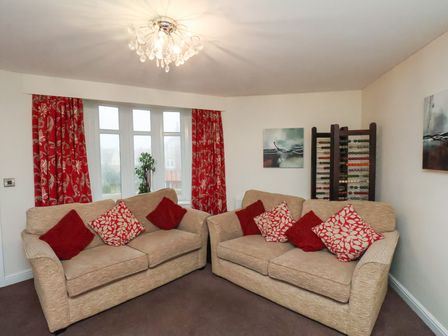 A living room with two beige sofas with red and patterned cushions near a window with red curtains at Counting House in Bridlington
