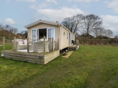 A mobile home with a wooden deck and outdoor seating on a grassy field at Breathing Space in Happisburgh near Walcott