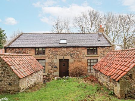 A stone cottage with a tiled roof and two small outbuildings with red tiled roofs at Timberwick Green in Akeld near Wooler