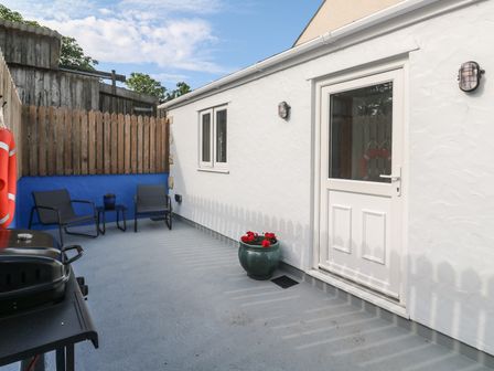 An outdoor patio area with two chairs a table flower pots a barbecue grill and a white door at The Stable in Rosudgeon