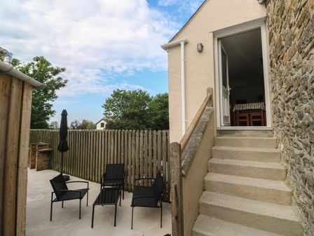 An outdoor patio with four black metal chairs and a table beside a staircase leading to an open door at Sea View Loft in Rosudgeon