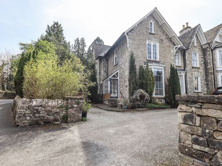 A stone house with trees and shrubs around it and a gravel driveway at The Parsonage in Kendal