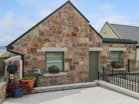 Exterior view of a stone house with two windows a door and flower pots at Ned's Cottage in Mulranny County Mayo