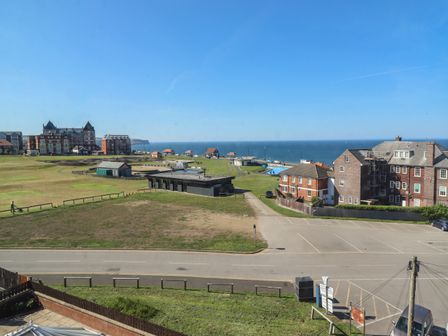 A coastal view with a grassy area, buildings, parking lot, and the sea at Mamoir's Place in Whitby