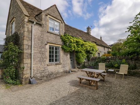 A stone house with a wooden picnic table and chairs outside surrounded by plants and a stone wall at The Stables at Daubeneys in Colerne