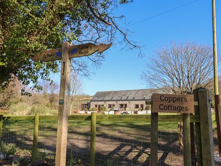 A wooden signpost showing directions to Penn and Lyme Regis near a stone building with windows and a fence at Coppers Cottages