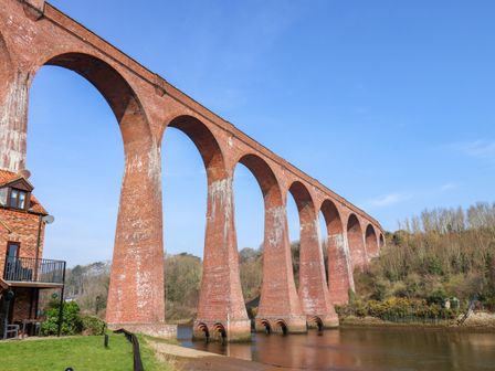 A brick railway viaduct crossing a river near a house and trees at No 18 Riverside Walk Kingfisher Whitby