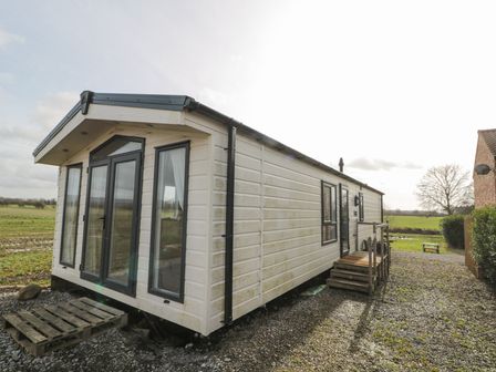 A white caravan with black framed windows and doors on a gravel driveway near fields at The Cosy Caravan in Islebeck near Thirsk