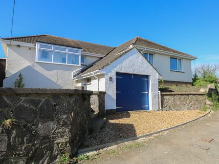 A house with a blue garage door and gravel driveway with stone walls at Arfryn in Solva