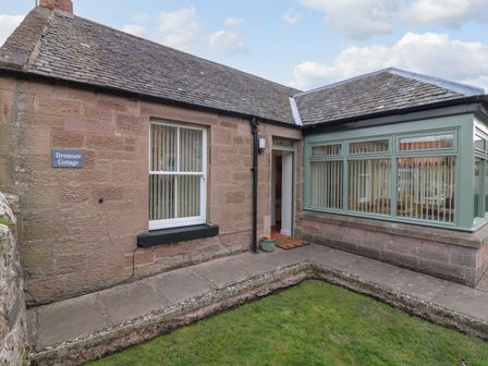 The exterior of a single-story stone cottage with a tiled roof and a small garden at Dromore Cottage in Norham