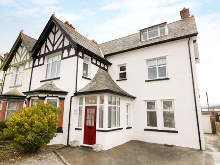 A semi detached house with white walls black trim and a red front door at 51 Trinity Avenue in Llandudno
