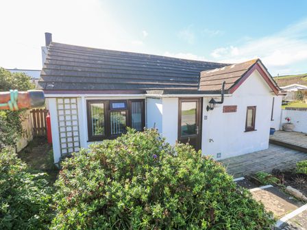 A white cottage with a dark roof surrounded by bushes and plants at Carolyns Cottage Praa Sands