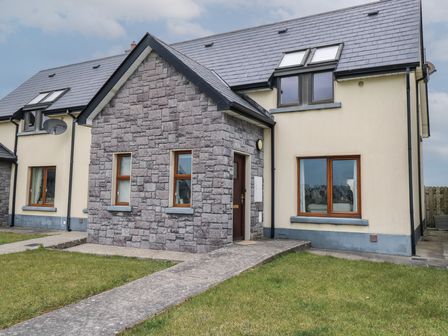A house with stone and cream walls with several windows and a pathway leading to the front door at C65 Cahermore Holiday Village in Enniscrone County Sligo