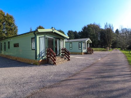 Two green mobile homes with steps and wooden railings on a gravel driveway surrounded by trees at Lodge 3 in Silverdale