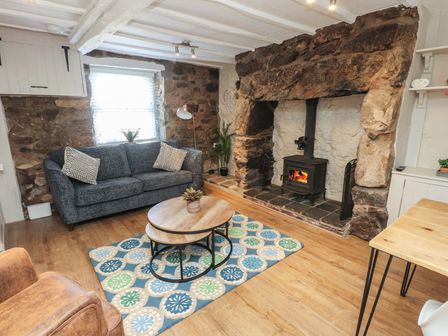 A living room with a blue sofa wooden tables a patterned rug a leather chair and a stone fireplace with a wood stove at Hafod in Llanbedrog