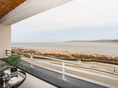 A balcony with a table holding a plant and tea set overlooking a beach and sea at 2 The Quay in Pentraeth