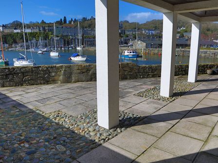 A marina with several boats docked near a stone wall and a covered patio with white pillars at Glaslyn Harbour Views in Porthmadog
