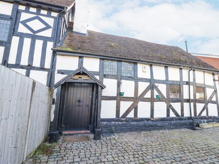 A black and white timber framed house with a cobblestone courtyard and a black door at Wyre Court Cottage in Bewdley
