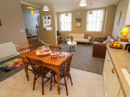 A dining table with four wooden chairs and food on it next to a living room with two sofas a coffee table and windows at Cottage Annex in Constantine