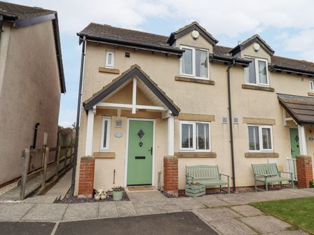A semi detached house with green front doors benches and flower pots outside at Tee View in Seahouses
