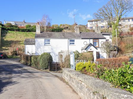A white terraced house with chimneys beside a road and stone wall surrounded by bushes at Minffordd in Pandy Tudur near Betws-Y-Coed
