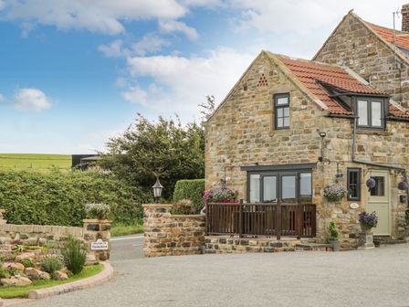 A stone cottage with tiled roof and flower pots near a road with a Yorkshire sign at The Hayshed in Normanby near Hawsker