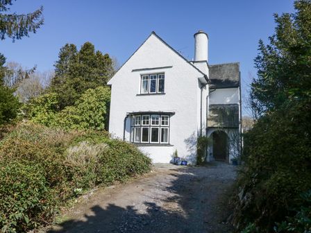 A white two-story house with a gravel driveway surrounded by greenery and trees at Brackenthwaite in Windermere