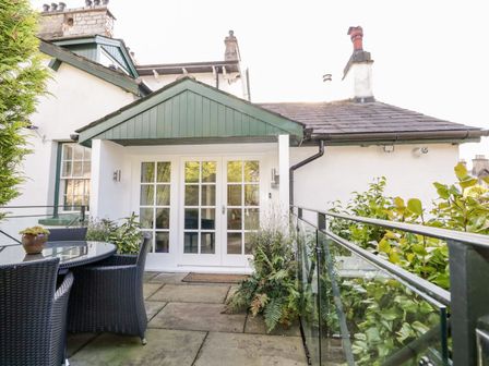 A patio with a round glass table and wicker chairs outside a white building with glass doors at The Bolt Hole in Kendal