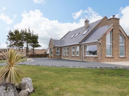 A suburban house with a stone exterior and a sloped roof surrounded by grass and trees at Radharc Na Tra near Burtonport County Donegal